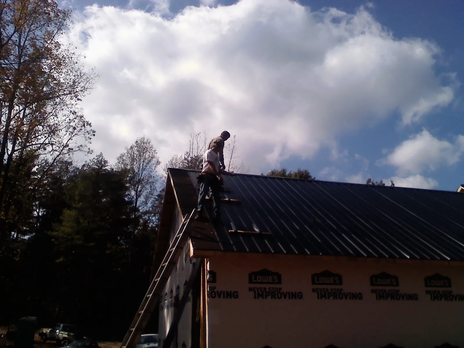 Roofer fastening dark metal panels high against a cloudy sky, from a Roof Inspection job in Mechanicsburg