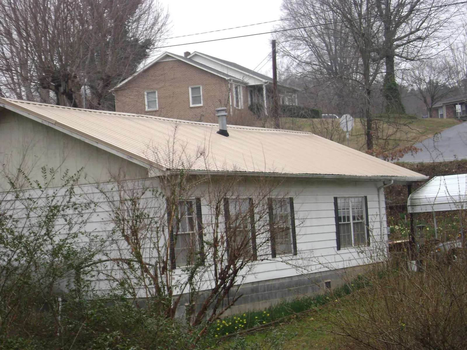Tan metal roof on a white sided house set into a hillside — Commercial Roofing by Roofing Brothers in Mechanicsburg